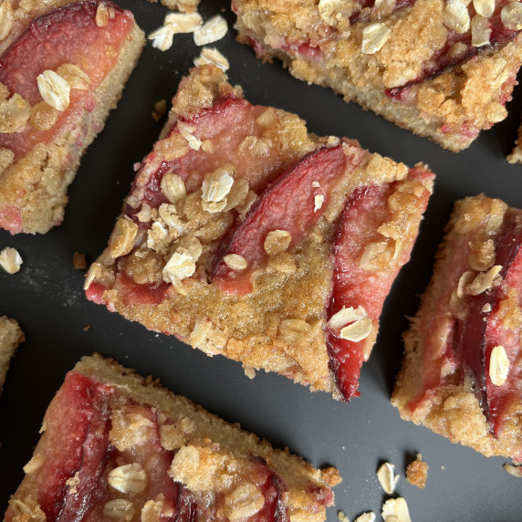 Snack cake topped with red plums arranged on a black countertop.