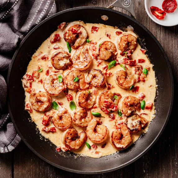 Seared shrimp in a creamy sun-dried tomato sauce, garnished with fresh basil and served in a black s
