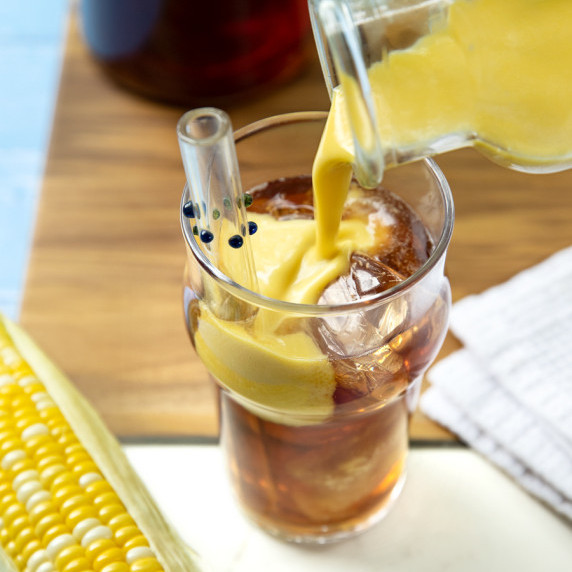 Pouring sweet corn milk into a glass of iced tea.