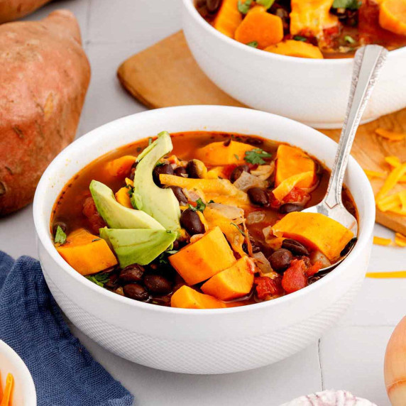 Serving of sweet potato black bean soup in a white bowl with a spoon.