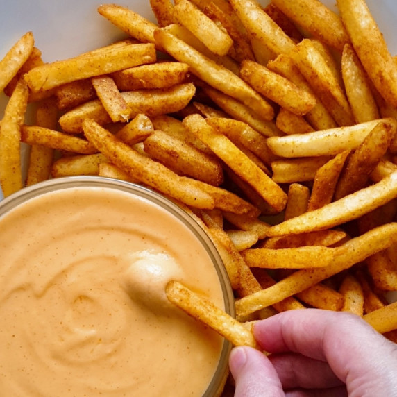 Copycat Taco Bell Nacho Fries Recipe, with a fry being dipped in nacho cheese sauce.