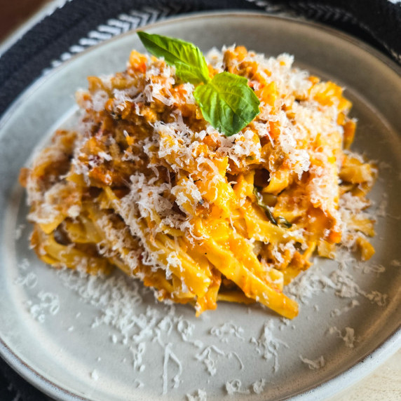 An orange nest of tagliatelle with green basil on a white rimmed bowl.