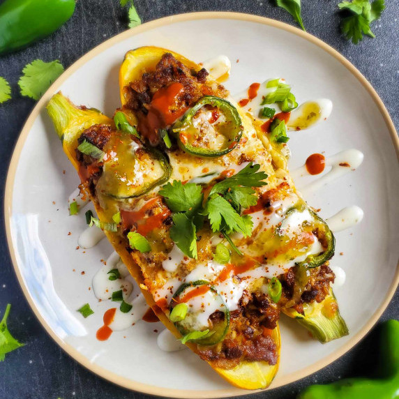 a colourful, stuffed zucchini on a white plate against a black cutting board