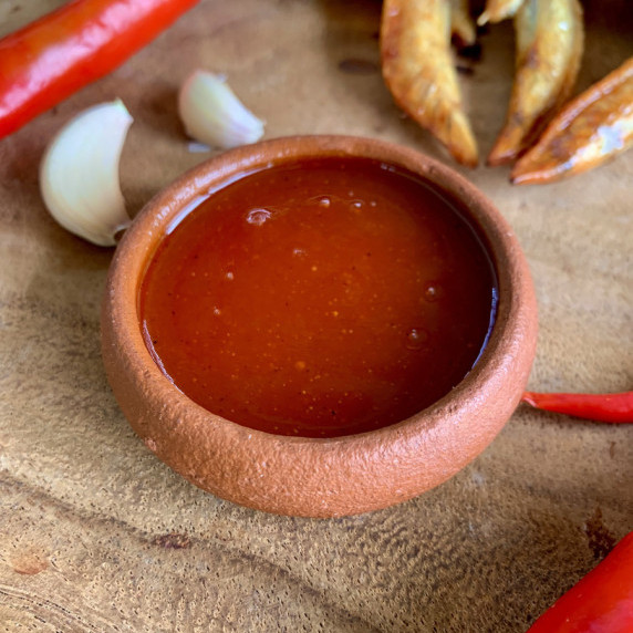 Thai hot sauce / sriracha sauce in a clay cup with garlic, chilies, and fried chicken around it.