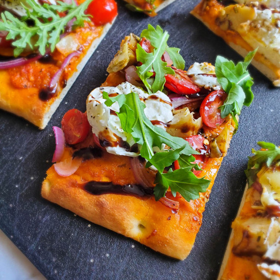 Crispy, golden flatbread topped with fresh green arugula and creamy burrata with a black background.