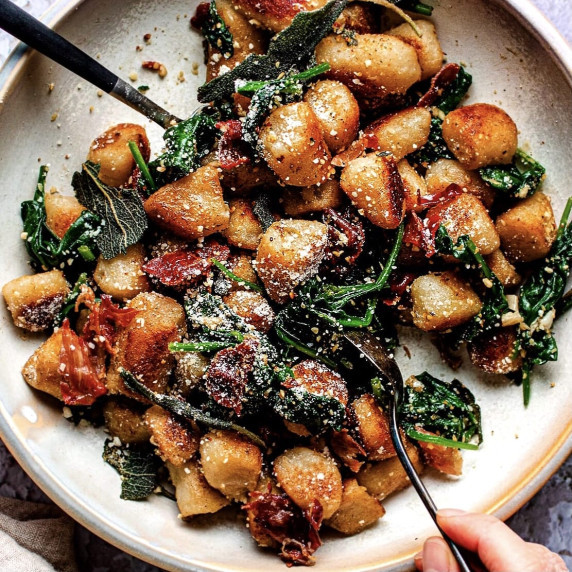 Gnocchi, prosciutto, spinach and parmesan cheese on a white plate with two spoons