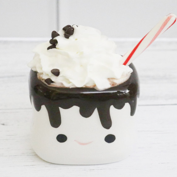 Hot chocolate with whipped cream, mini chocolate chips, and a candy cane spoon in a cute mug.