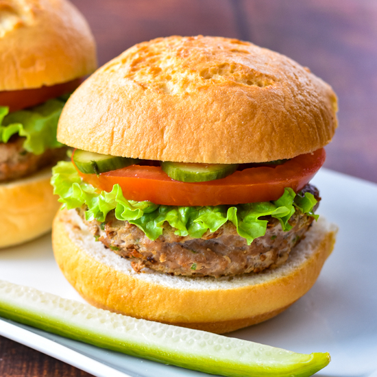a turkey burger on a gluten-free bun topped with pickles, tomato and lettuce on a white plate