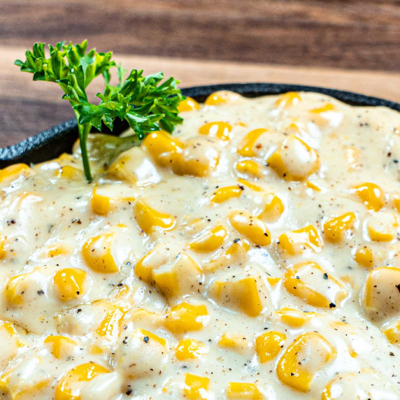 Creamed Corn in a cast iron skillet with a parsley sprig