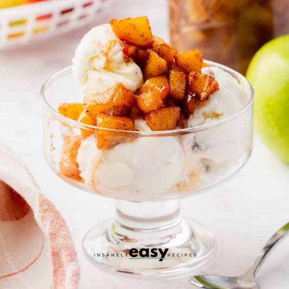 Apple compote served with vanilla ice cream in an ice cream glass, a spoon & green apple next to it