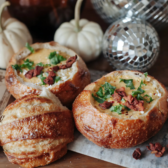 Three sourdough bread bowls filled with creamy broccoli cheese soup, garnished with fresh parsley an