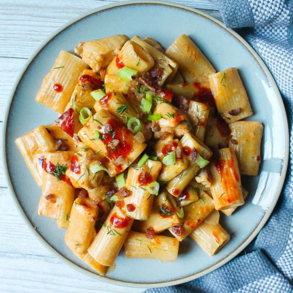 blue plate with creamy chipotle pasta topped with fresh dill, green onion, adobo sauce