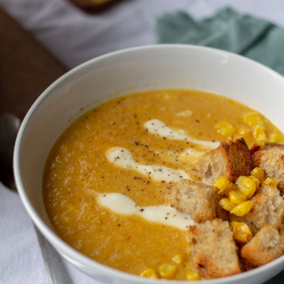 Bowl of orange corn and bell pepper soup with sourdough croutons