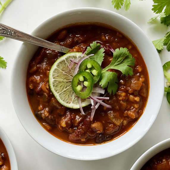 Bowl of vegetarian chili topped with sliced jalapenos, lime, and red onion on a white countertop.