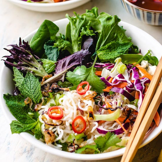 Shirataki noodles, mixed greens, red chili pepper and purple cabbage in white bowl with chopsticks