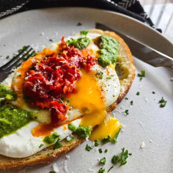 Toast topped with a golden, runny yolk, green pesto, and red pepperoncini.