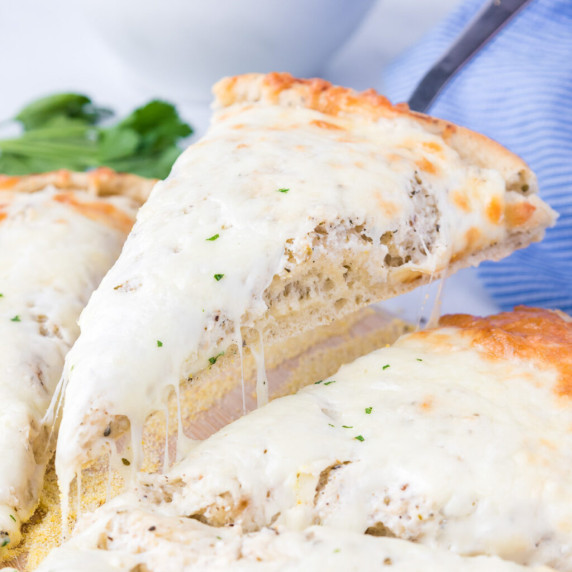 Close up view of a slice of white pizza being pulled up from the whole pie pulling the melty cheese.