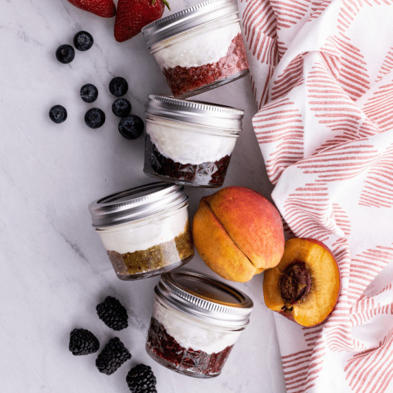 Small jelly jars with fruit on the bottom and yogurt on top arranged on a counter with fresh fruit.