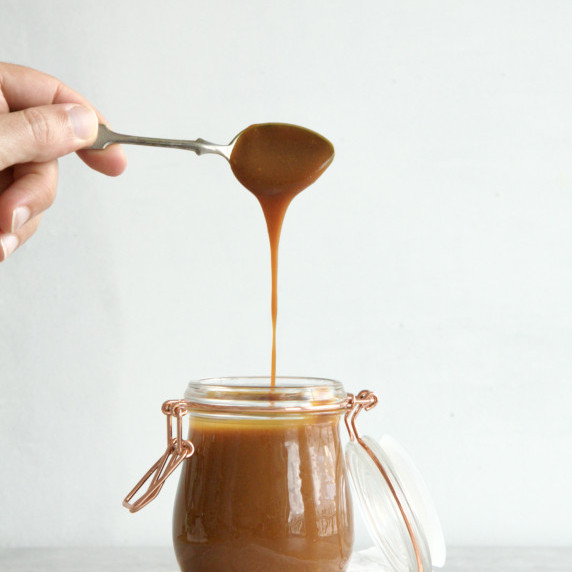 Glass jar filled with vanilla caramel sauce with caramel sauce dripping from a spoon