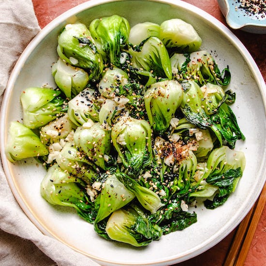 Stir fried bok choy, garlic, sesame seeds and red pepper flakes in a white bowl 