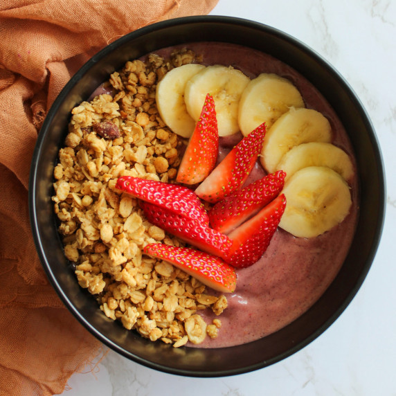 An acai smoothie bowl topped with strawberries, banana, and granola