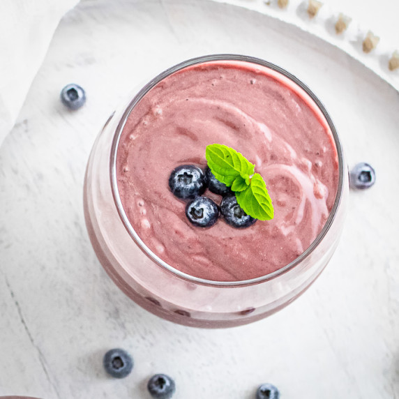 Overhead shot of acai smoothie garnished with blueberries and mint in a clear glass on a white table