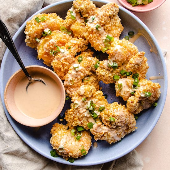 Air fried shrimp and scallions on a plate with bang bang sauce in ramekin with spoon