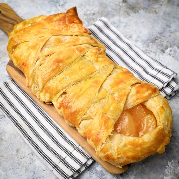 Side close up shot of criss-crossed apple danish on a small cutting board on a striped table cloth.