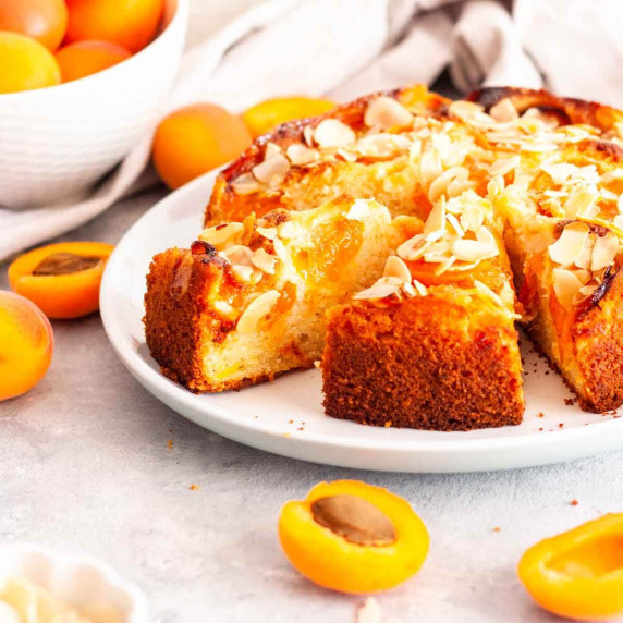Sliced apricot almond cake on a white plate next to fresh apricots.