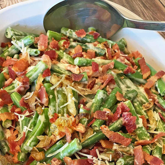 A silver serving spoon with bacon topped green bean casserole.
