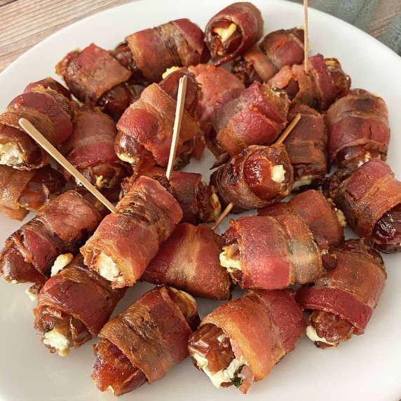 Two dozen bacon wrapped dates on a white serving dish. 