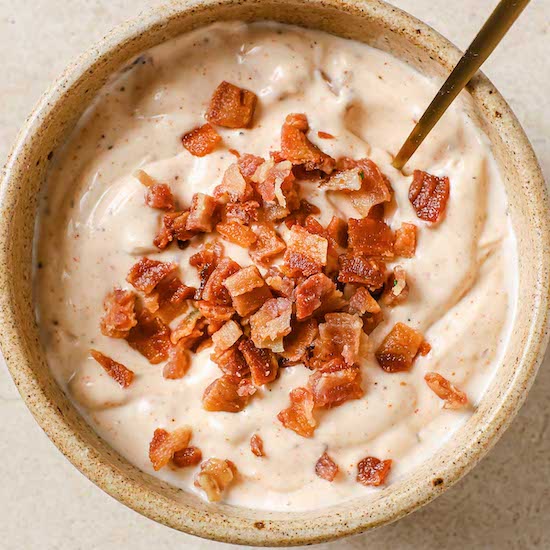 Bacon aioli with bacon bits in a stoneware ramekin with spoon