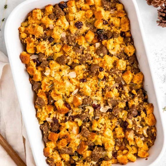 A white baking dish filled with golden, baked sausage and cornbread dressing with dried cranberries.