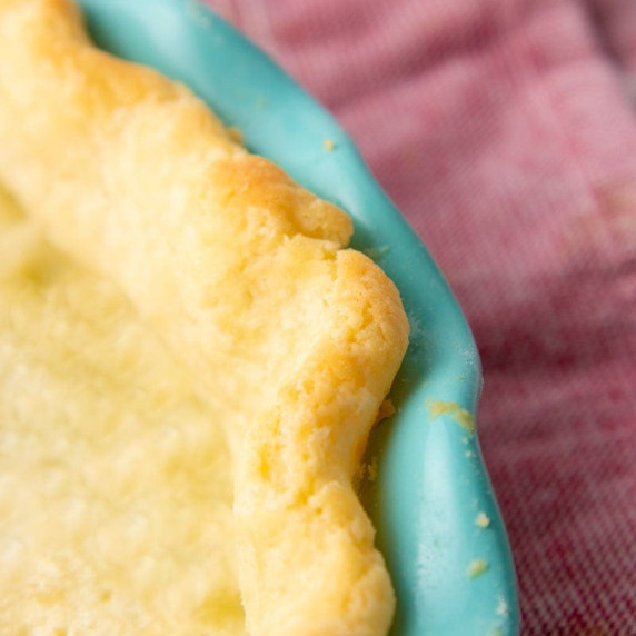 Close view of a golden, baked gluten-free pie crust around the edge of a teal pie plate.