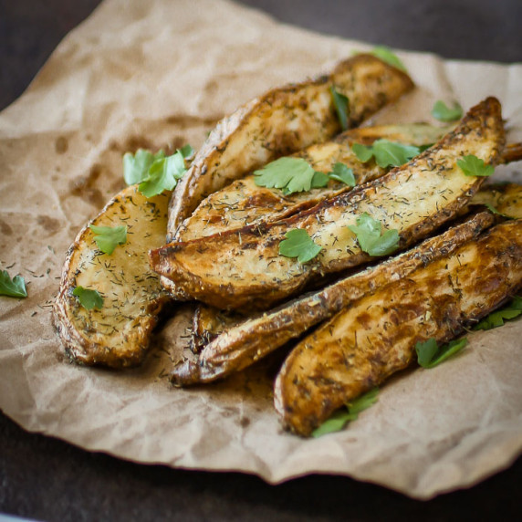 Side close up shot of multiple dill French fries garnished with herbs on a brown paper.