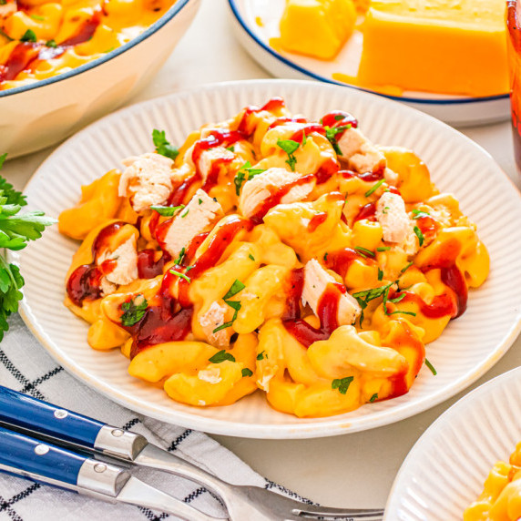 a plate of mac and cheese topped with chicken, bbq sauce, and parsley on a white plate. 