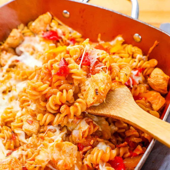 a spoon lifting out bbq chicken pasta with tomatoes and mozzarella cheese.