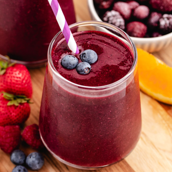 A beet spinach smoothie in a glass with a straw and three blueberries on top.
