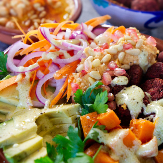 a rice bowl loaded with beetroot falafels, grated carrot, avocado, pine nuts, and hummus