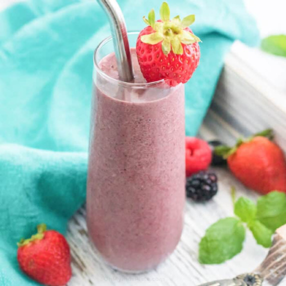 Close up of smoothie in a glass with berries garnishing and around the smoothie.