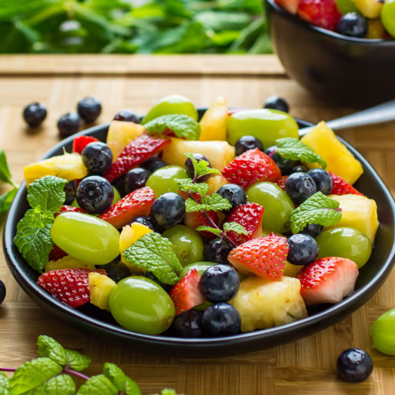 Side shot of berry fruit salad with a mint garnish on a black plate.