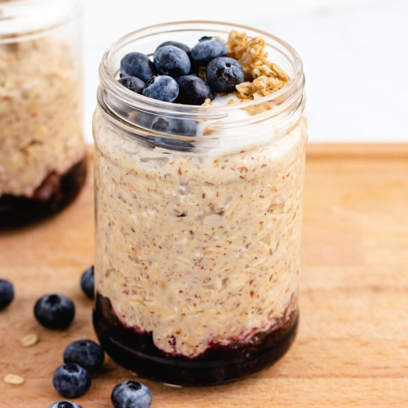 Blueberry cheesecake overnight oats layered in a jar with blueberries on the bottom.