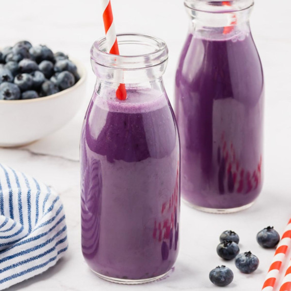 Blueberry milk in two glasses with straws, some fresh blueberries on the sides
