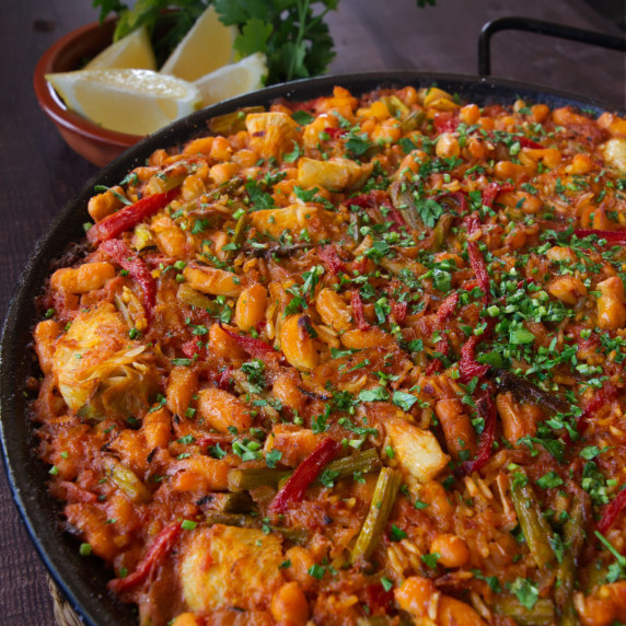 a large pan of Spanish oven-baked rice sits beside a bowl of lemon wedges
