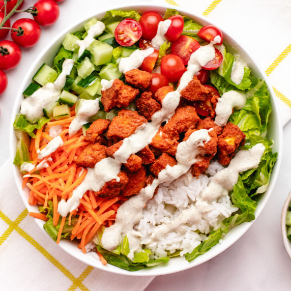 Buffalo tofu rice bowl with carrots, tomatoes, cucumbers, lettuce, and a dairy-free ranch.