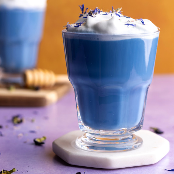 Butterfly pea latte in glass mug with edible flowers on top