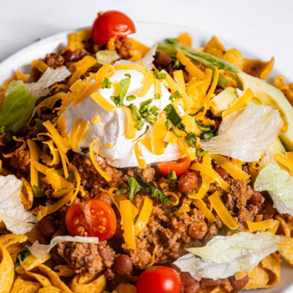Frito corn chips piled with a beef mixture and toppings on top.