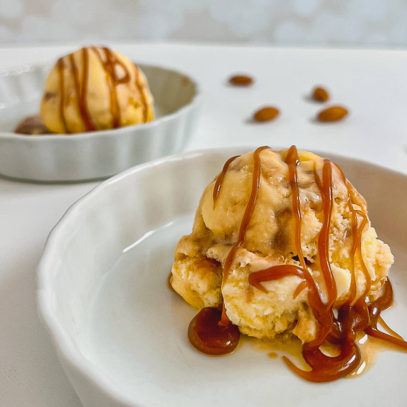 One scoop of Caramel Swirl Almond Gelato drizzled with caramel sauce in a white bowl with another bo
