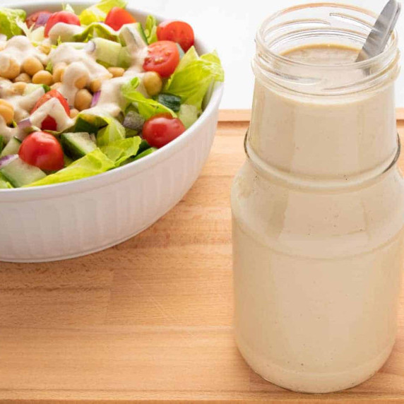 Cashew dressing in a jar with a spoon and a salad in the background.