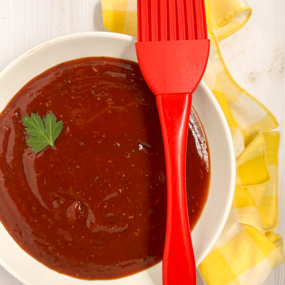 A round white bowl filled with Cajun bbq sauce with a red baster resting on the side. 